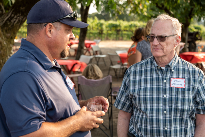 man drinking wine talking to other man with nametag